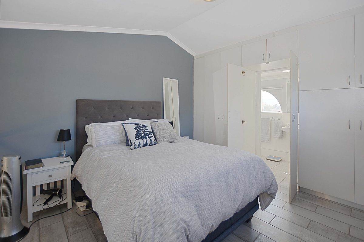 A well-maintained bedroom featuring built-in cupboards, tiled flooring, and a vaulted ceiling, with direct access to an en-suite bathroom.