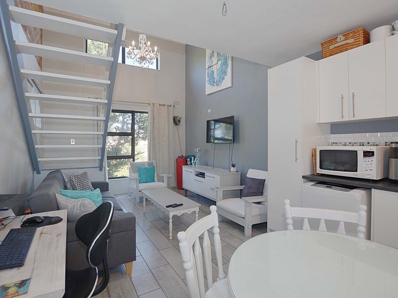 Open-plan living area featuring a modern staircase, tiled flooring, and a compact kitchen with built-in cabinetry, creating a bright and functional living space.