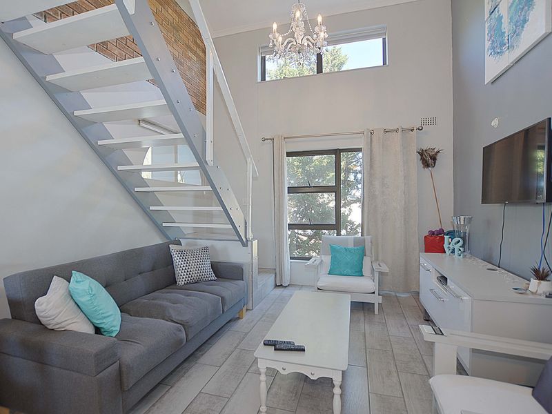 A bright living room featuring a modern staircase, exposed brick accents, and large windows that provide ample natural light.