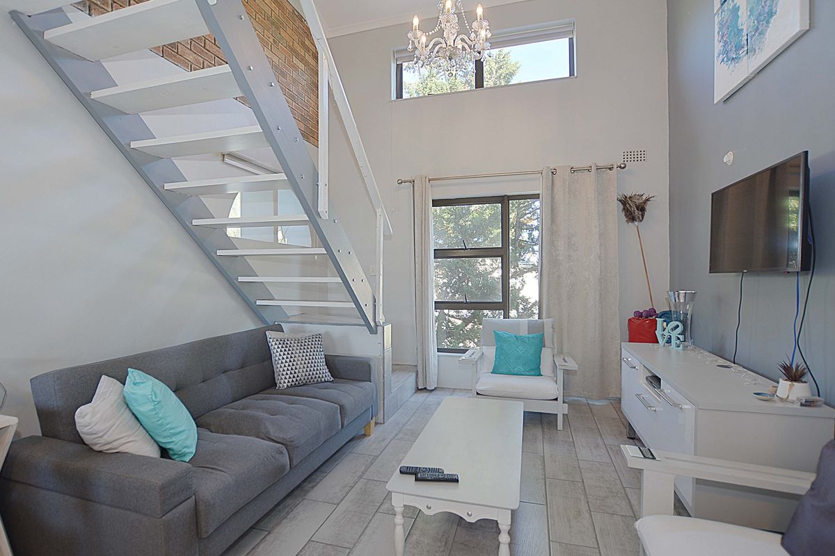A bright living room featuring a modern staircase, exposed brick accents, and large windows that provide ample natural light.