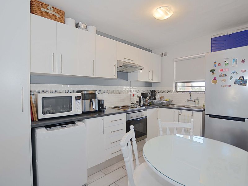 A functional kitchen featuring white cabinetry, tiled backsplash, built-in oven, cooktop, and stainless steel sink, with tiled flooring throughout.