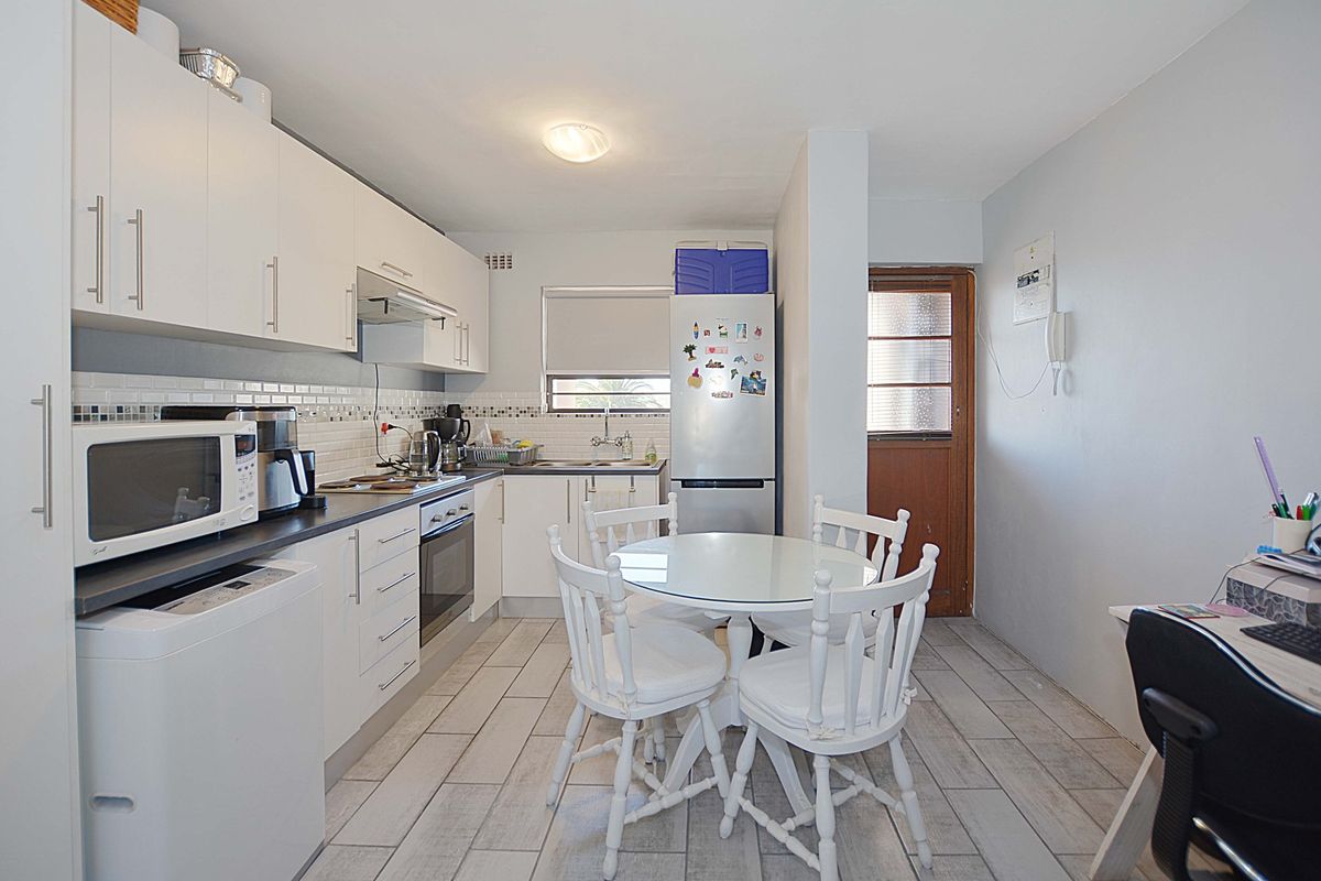 Functional kitchen featuring white cabinetry, tiled backsplash, built-in oven, and direct access to an external door, with adjacent dining area.