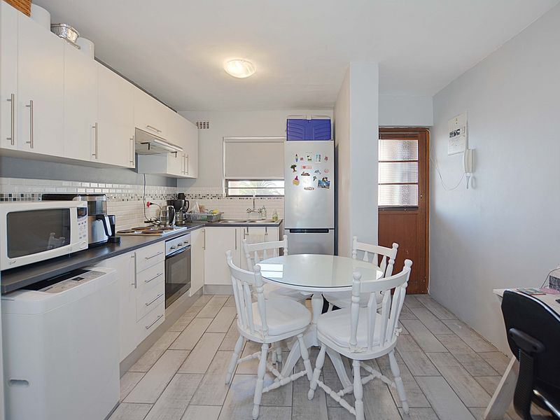 Functional kitchen featuring white cabinetry, tiled backsplash, built-in oven, and direct access to an external door, with adjacent dining area.