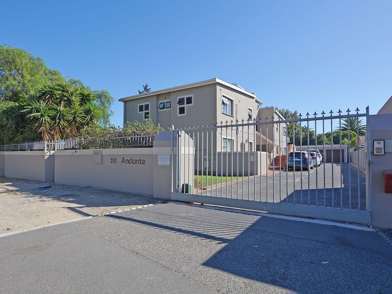 Front view of the apartment complex entrance featuring a secure metal gate, perimeter wall, and paved driveway access.