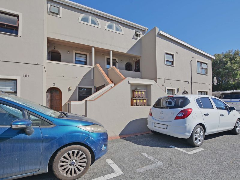 Front elevation of a multi-story apartment complex featuring external staircases, balconies, and communal post boxes in a paved parking area.