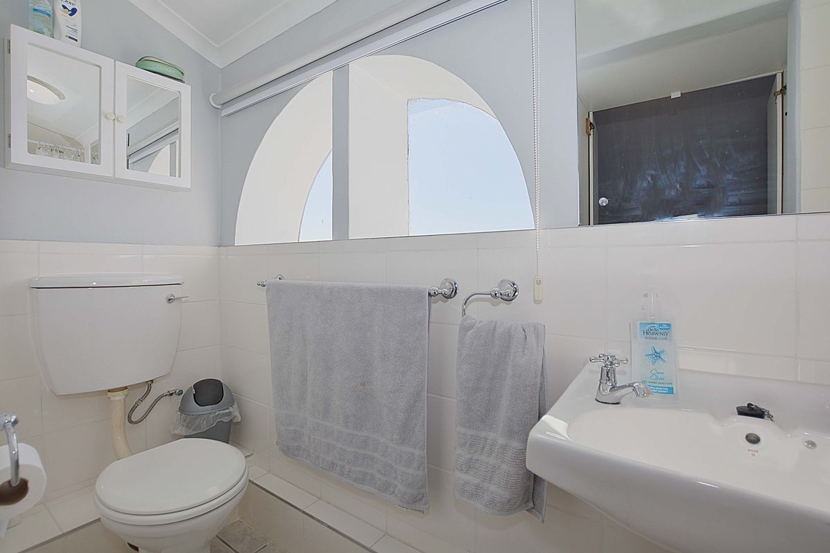 A functional bathroom featuring a wall-mounted basin, toilet, and arched window, finished with white wall tiles and a wall-mounted medicine cabinet.