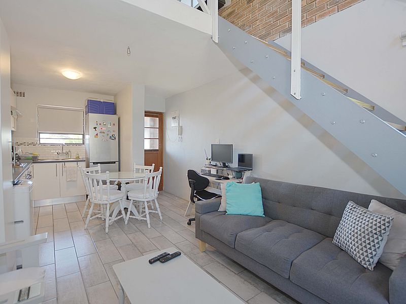 Open-plan living area featuring a staircase, exposed brick wall, and a functional kitchen with tiled flooring throughout.