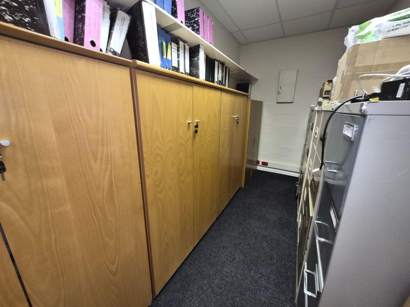 A functional utility or storage room featuring carpeted flooring, suspended ceiling tiles, and integrated electrical trunking for office infrastructure.