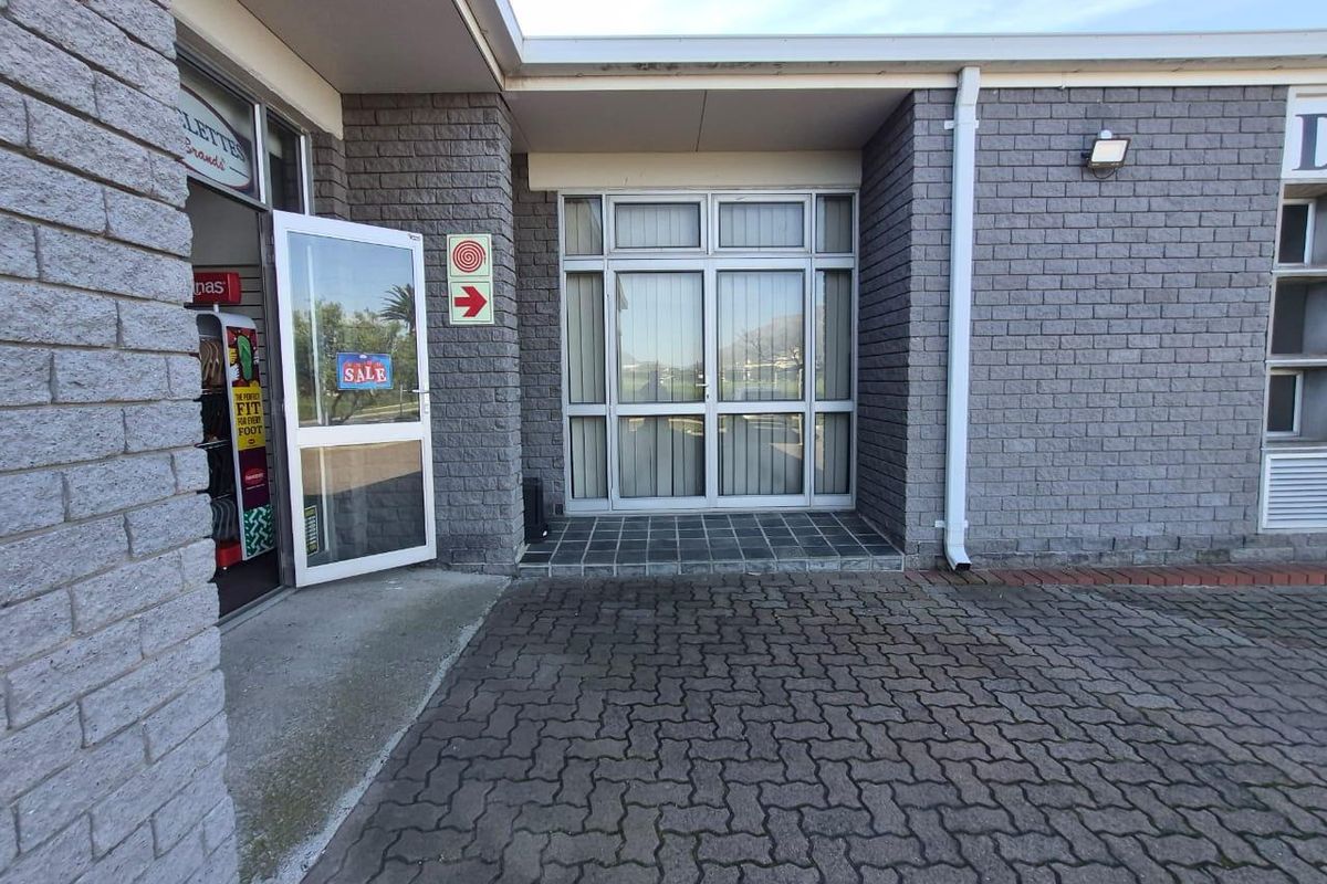 Commercial building entrance featuring a paved approach, brick facade, and aluminium-framed glass doors.