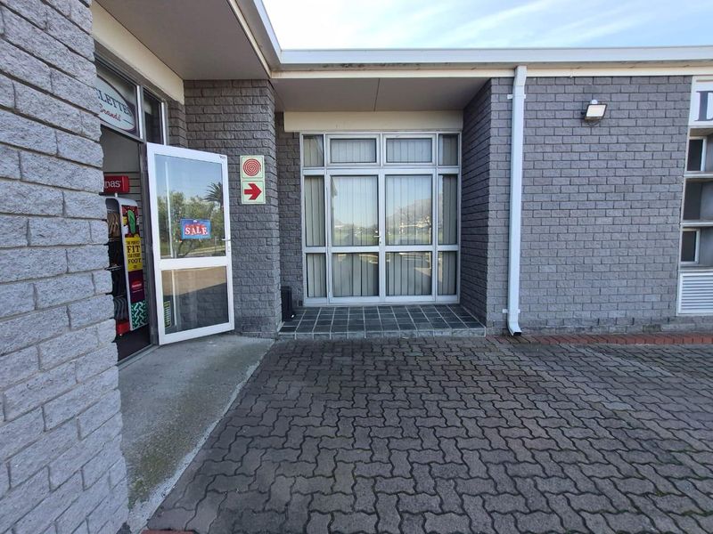 Commercial building entrance featuring a paved approach, brick facade, and aluminium-framed glass doors.