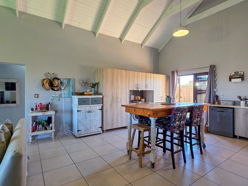 Spacious open-plan living and kitchen area featuring a high vaulted ceiling, tiled floors, modern built-in cabinetry, and direct access to the outdoor space.