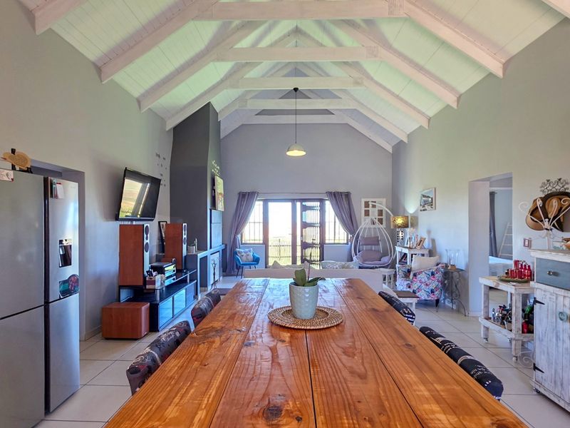 Spacious open-plan living and dining area featuring a high vaulted ceiling with exposed timber trusses, tiled floors, and a built-in fireplace.