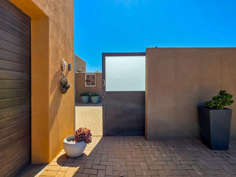 A well-maintained front entrance area featuring a paved driveway, a modern pedestrian gate with frosted glass, and a garage door.