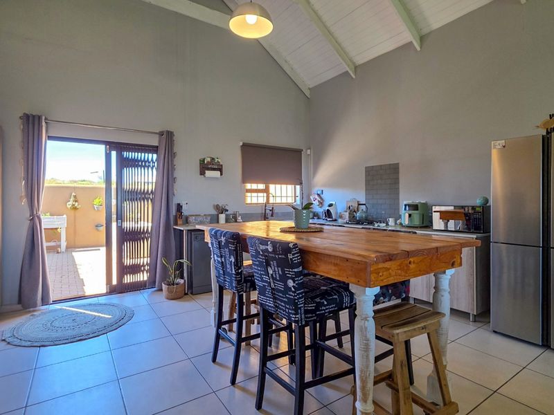 Open-plan kitchen and living area featuring vaulted ceilings, tiled floors, and direct access to an outdoor patio through a sliding glass door.
