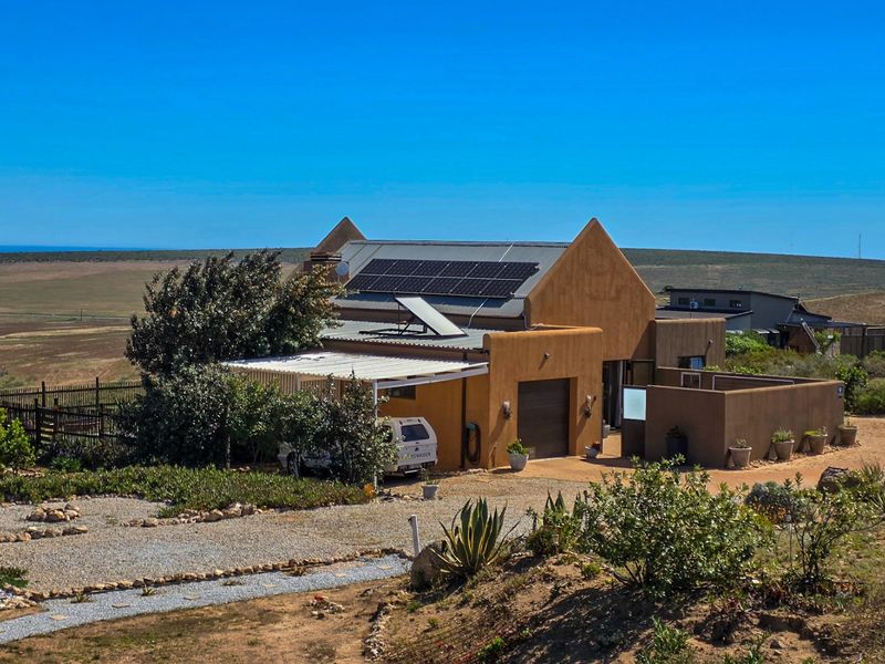 Front view of a modern house featuring solar panels, a solar geyser, a garage, and a covered carport, set in a scenic landscape.