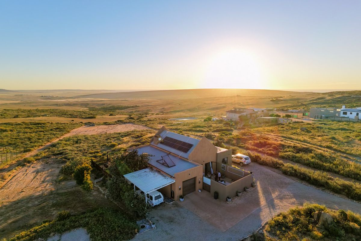 Aerial view of a rural property featuring a house with solar panels, a metal roof, and a large surrounding landscape at sunset.