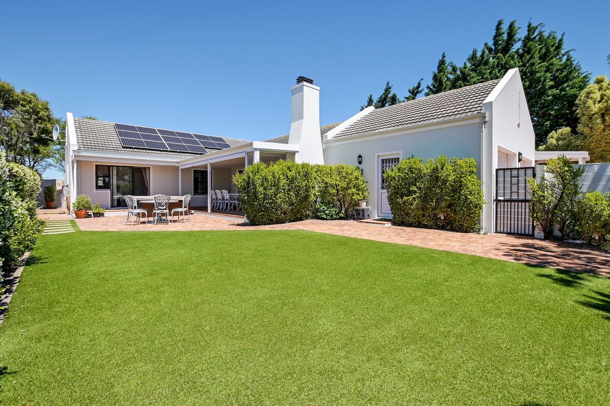 Rear view of the property featuring a well-maintained garden, artificial lawn, brick paved patio, covered outdoor area, and roof-mounted solar panels.