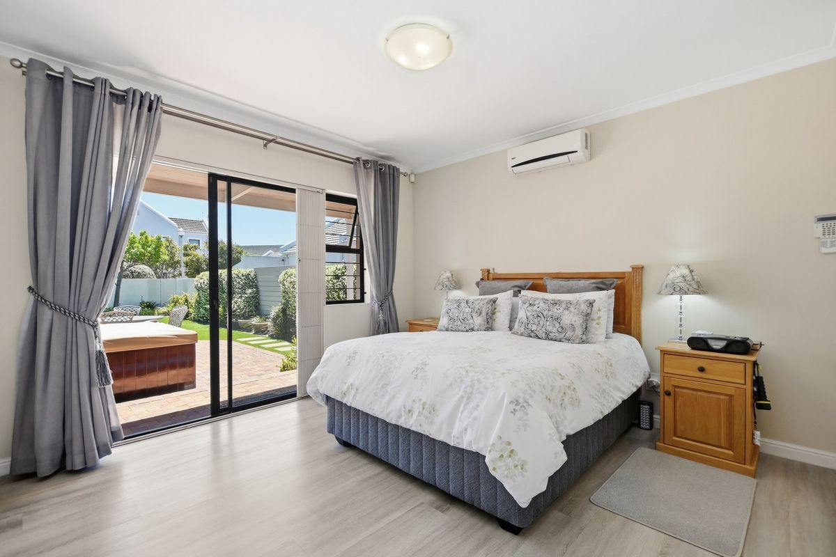 Spacious bedroom featuring light laminate flooring, a split-system air conditioner, and large sliding glass doors providing direct access to the rear patio and garden.