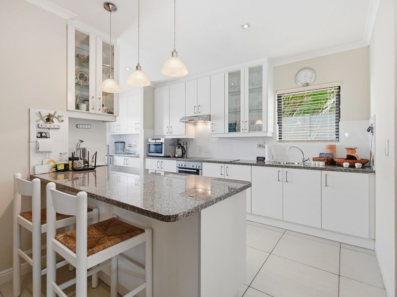 Modern kitchen featuring white cabinetry, granite countertops, a central island with breakfast bar seating, and integrated stainless steel appliances.