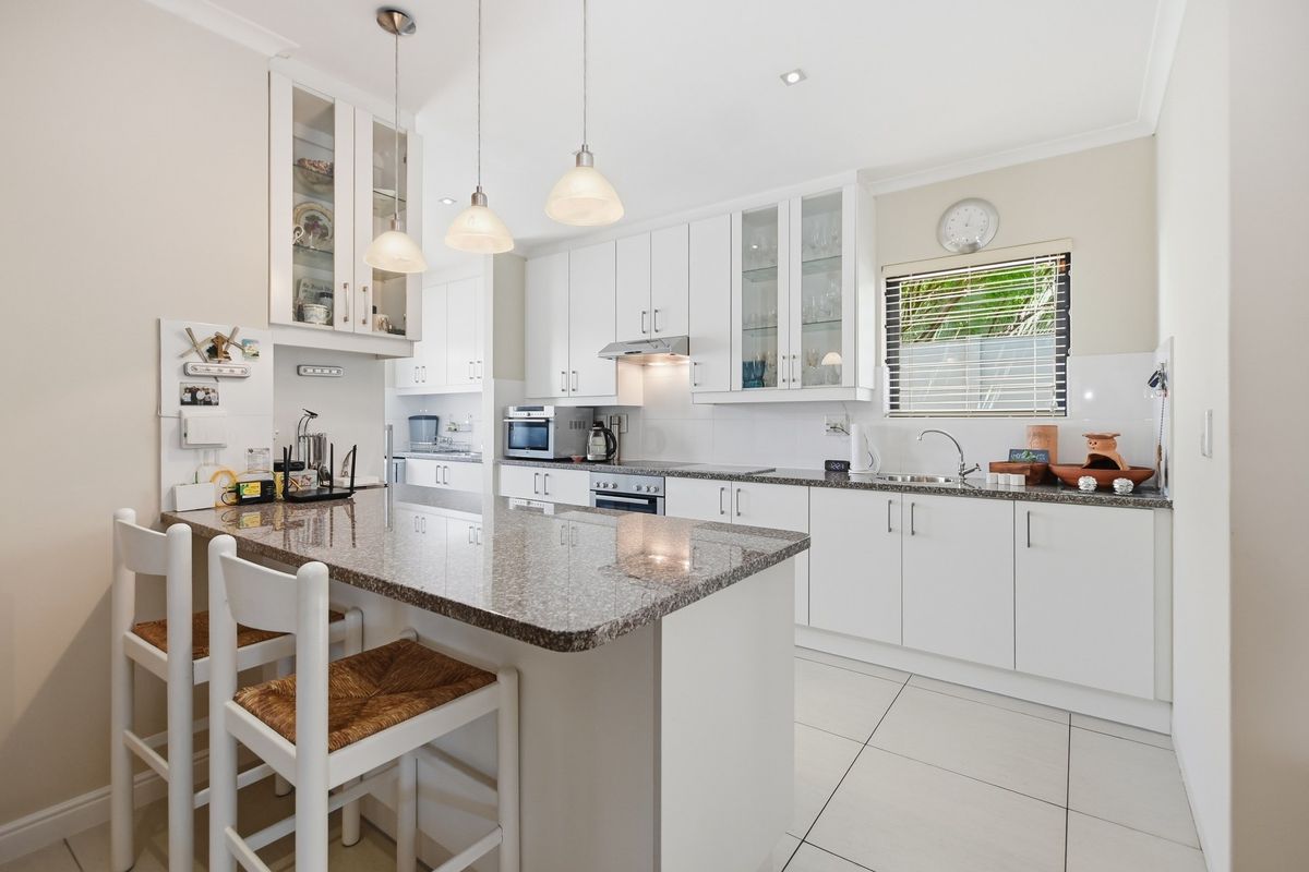 Modern kitchen featuring white cabinetry, granite countertops, a central island with breakfast bar seating, and integrated stainless steel appliances.