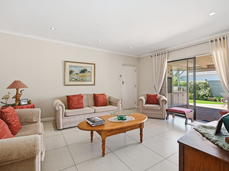 A bright and well-maintained living room featuring neutral tiled flooring, recessed downlighting, and direct access to an outdoor patio area through sliding glass doors.