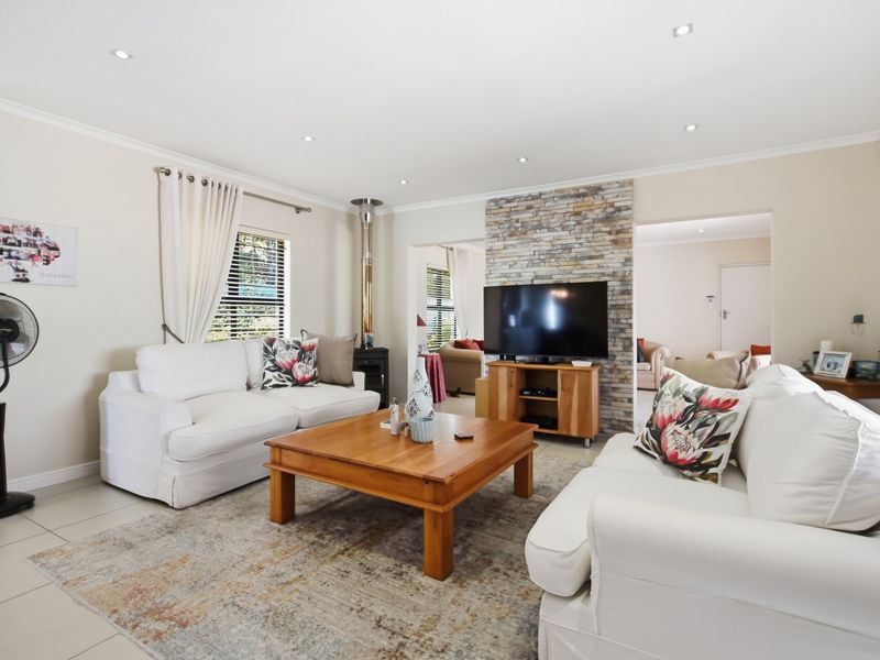 A bright and spacious living room featuring a stone-clad feature wall, tiled flooring, recessed downlighting, and a modern wood-burning stove.