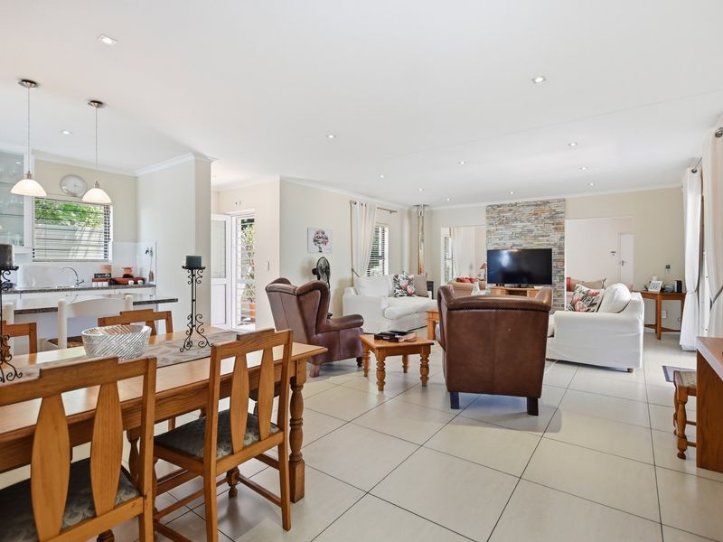 Spacious open-plan living area featuring a stone-clad fireplace, tiled flooring, and a modern kitchen with an island, creating a bright and functional family space.