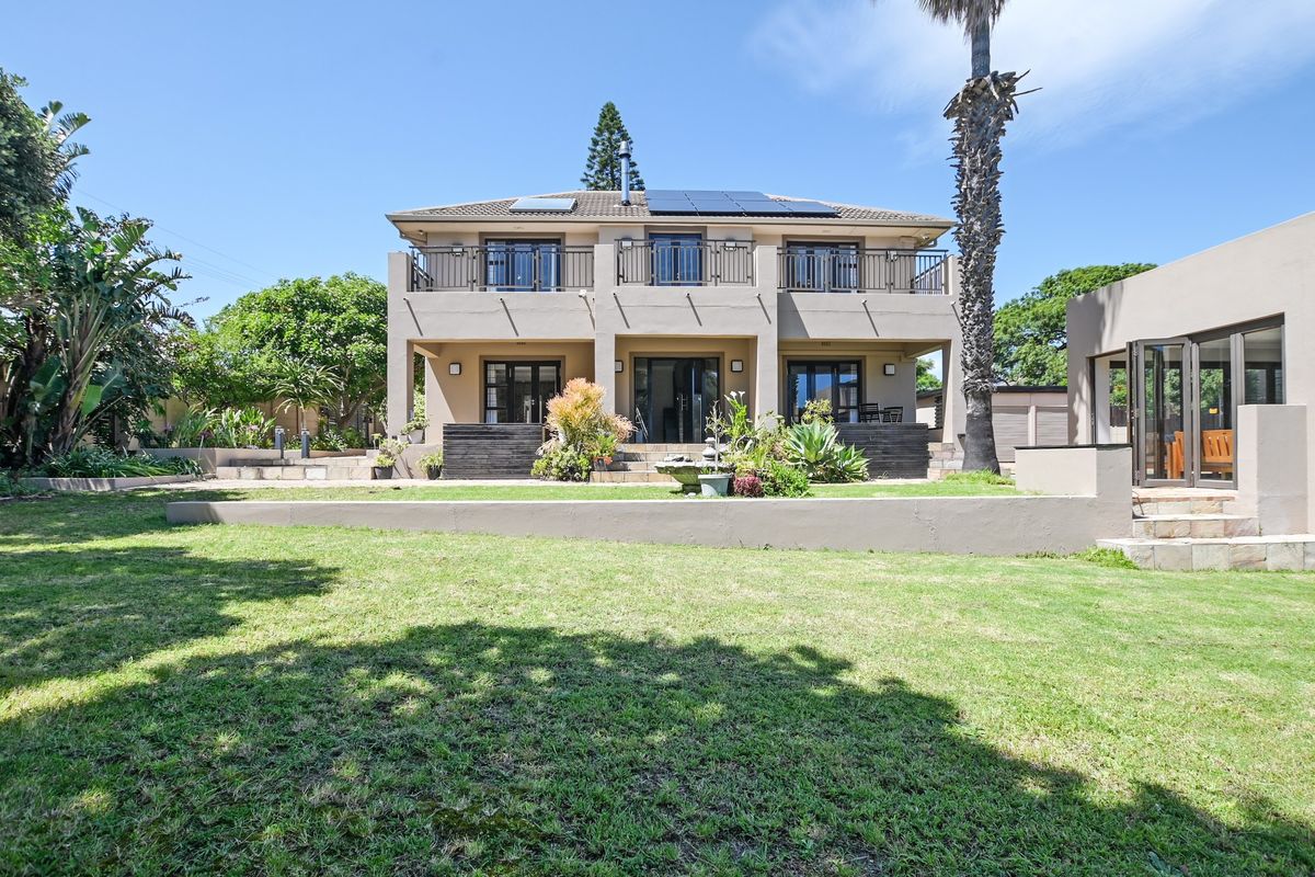 Rear view of a two-story house featuring a landscaped garden, a raised patio area, balcony with metal railings, and roof-mounted solar panels.