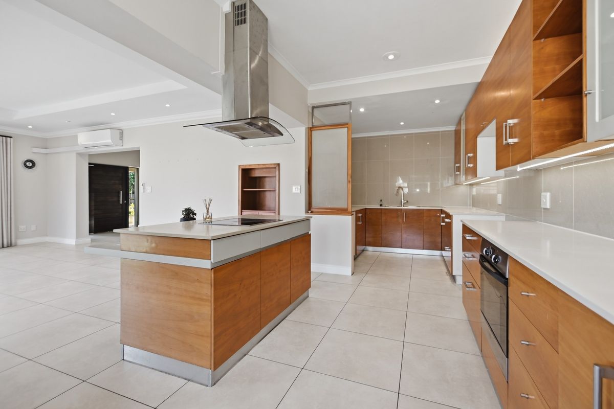 Modern kitchen featuring a central island with a built-in hob, stainless steel extractor fan, ample wooden cabinetry, and sleek stone countertops.