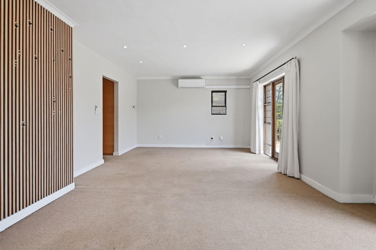 A spacious, light-filled living room featuring neutral carpeting, a modern timber slat feature wall, and direct access to an outdoor area via sliding doors.