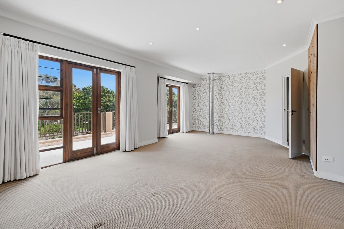Spacious bedroom featuring neutral carpet, feature wallpaper, built-in wardrobes, and dual sets of french doors opening onto a balcony.