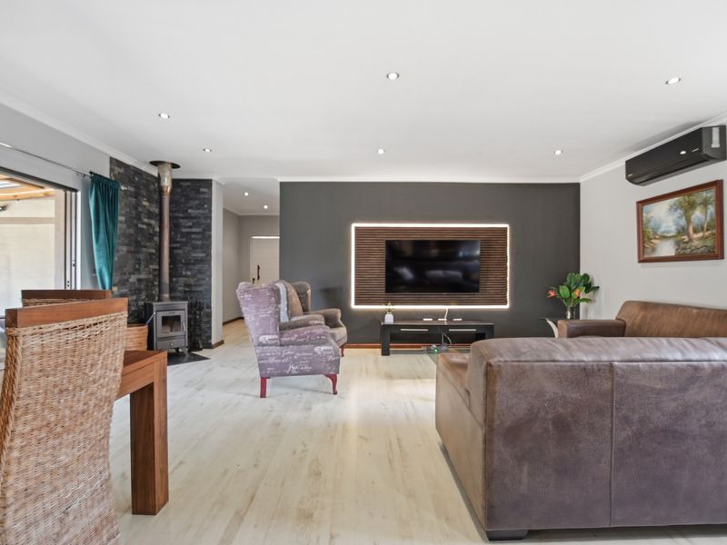 Spacious living room featuring a stone-clad wood-burning fireplace, modern accent wall with integrated lighting, and light-toned laminate flooring with direct patio access.