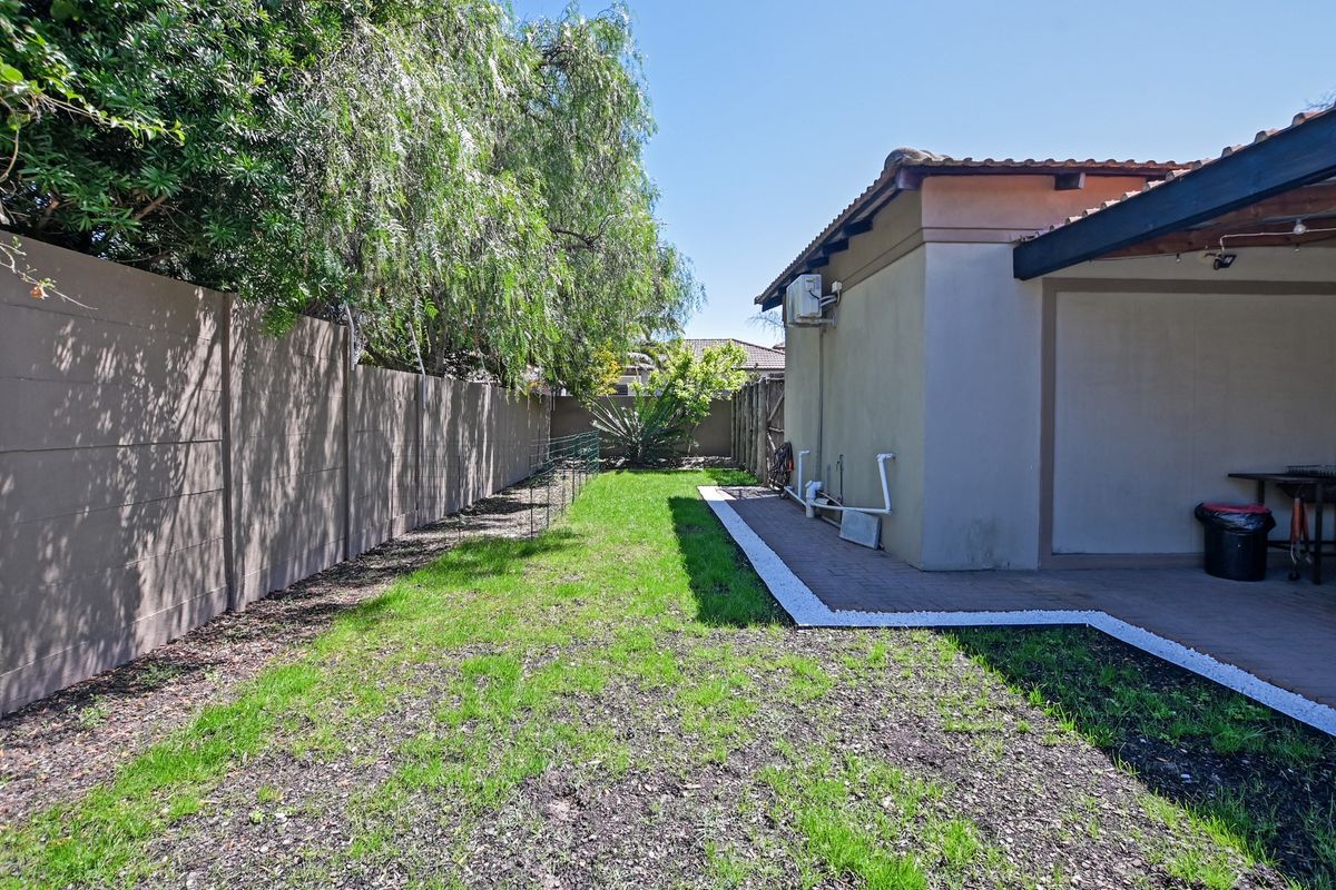 A rear garden area featuring a paved patio, boundary wall, and established trees, providing a private outdoor space adjacent to the main dwelling.