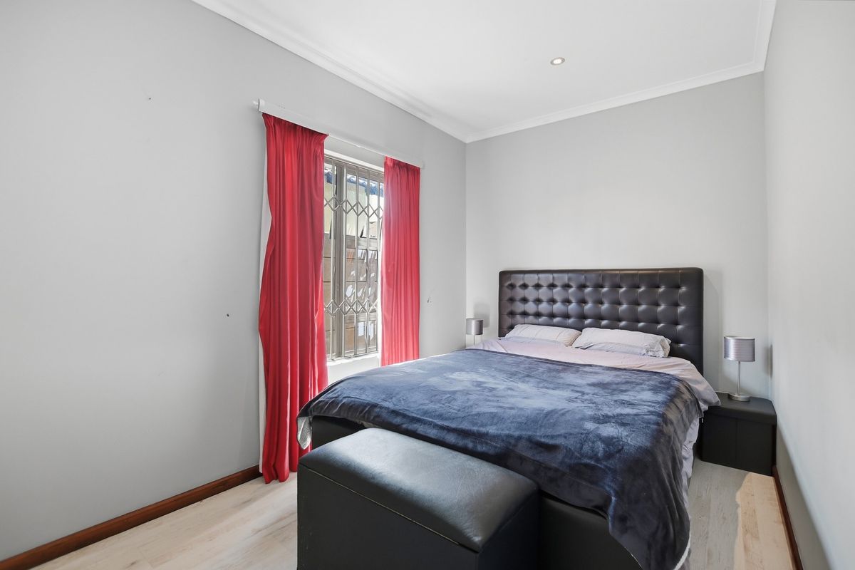A well-maintained bedroom featuring light-toned laminate flooring, recessed ceiling lighting, and a secure window with fitted security gate.