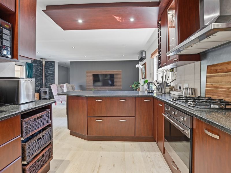 Spacious open-plan kitchen and living area featuring dark wood cabinetry, granite countertops, integrated appliances, and a cozy wood-burning fireplace in the lounge.