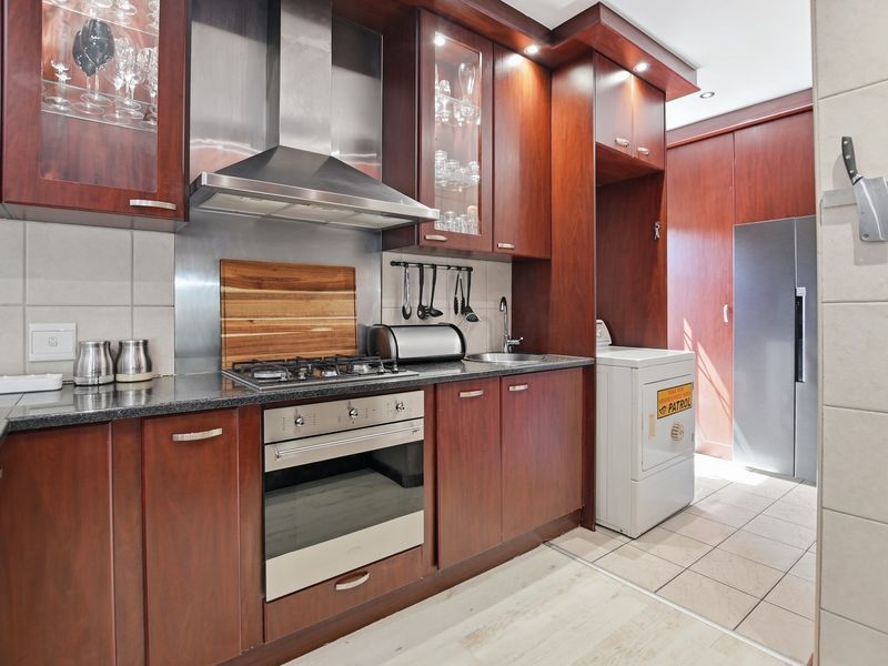 A well-appointed kitchen featuring dark wood cabinetry, granite countertops, a gas hob, built-in oven, and integrated stainless steel extractor fan.