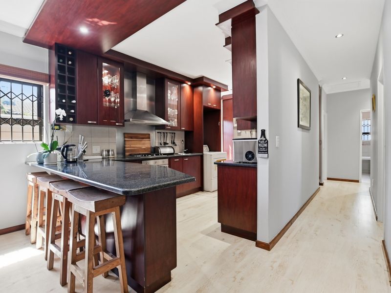 A well-maintained kitchen featuring dark wood cabinetry, granite countertops, a breakfast bar, and integrated stainless steel appliances, leading into a hallway.
