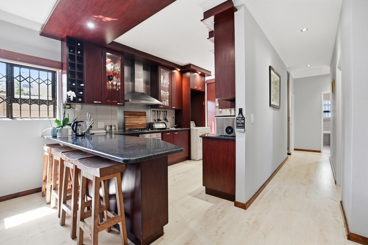 A well-maintained kitchen featuring dark wood cabinetry, granite countertops, a breakfast bar, and integrated stainless steel appliances, leading into a hallway.