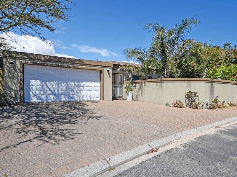 Front elevation of the property featuring a paved driveway, double garage, and secure boundary wall with electric fencing.