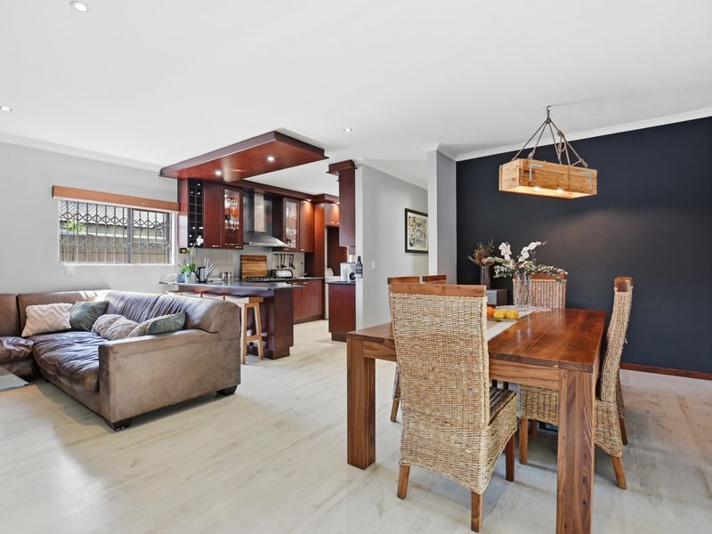 Spacious open-plan living and dining area featuring modern kitchen cabinetry, a central island, and light-toned laminate flooring, creating a cohesive and functional living space.