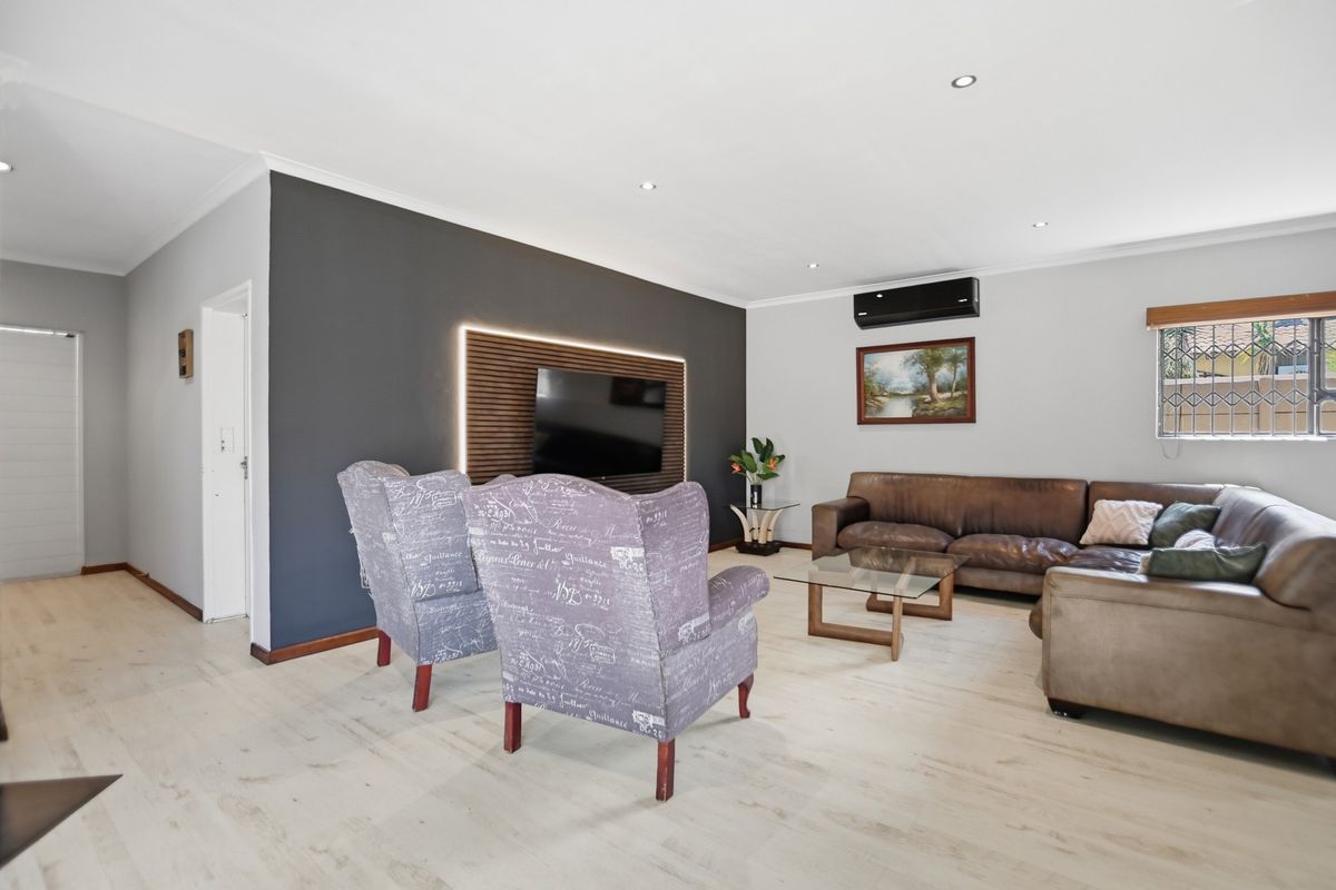 A well-maintained living room featuring light laminate flooring, a dark feature wall with integrated lighting, and a wall-mounted air conditioning unit.