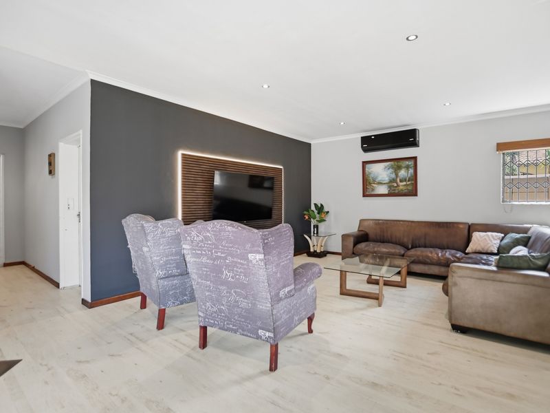 A well-maintained living room featuring light laminate flooring, a dark feature wall with integrated lighting, and a wall-mounted air conditioning unit.