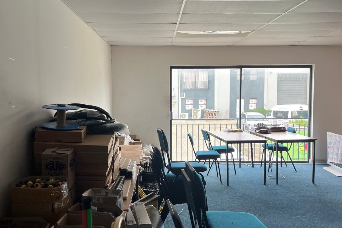 A commercial office space featuring a suspended ceiling, carpeted flooring, and a sliding glass door providing natural light and access to an exterior balcony.