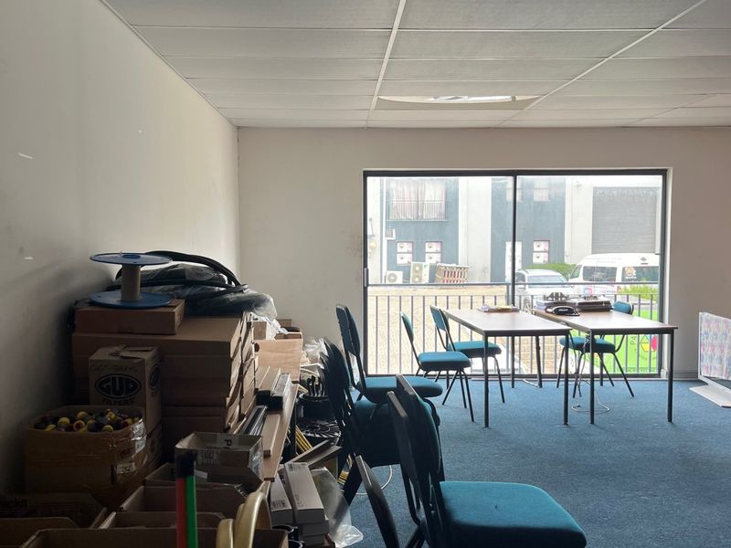 A commercial office space featuring a suspended ceiling, carpeted flooring, and a sliding glass door providing natural light and access to an exterior balcony.