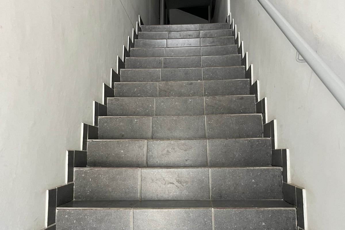 A functional interior staircase featuring dark tiled steps and a wall-mounted handrail, providing access between levels in a commercial property.