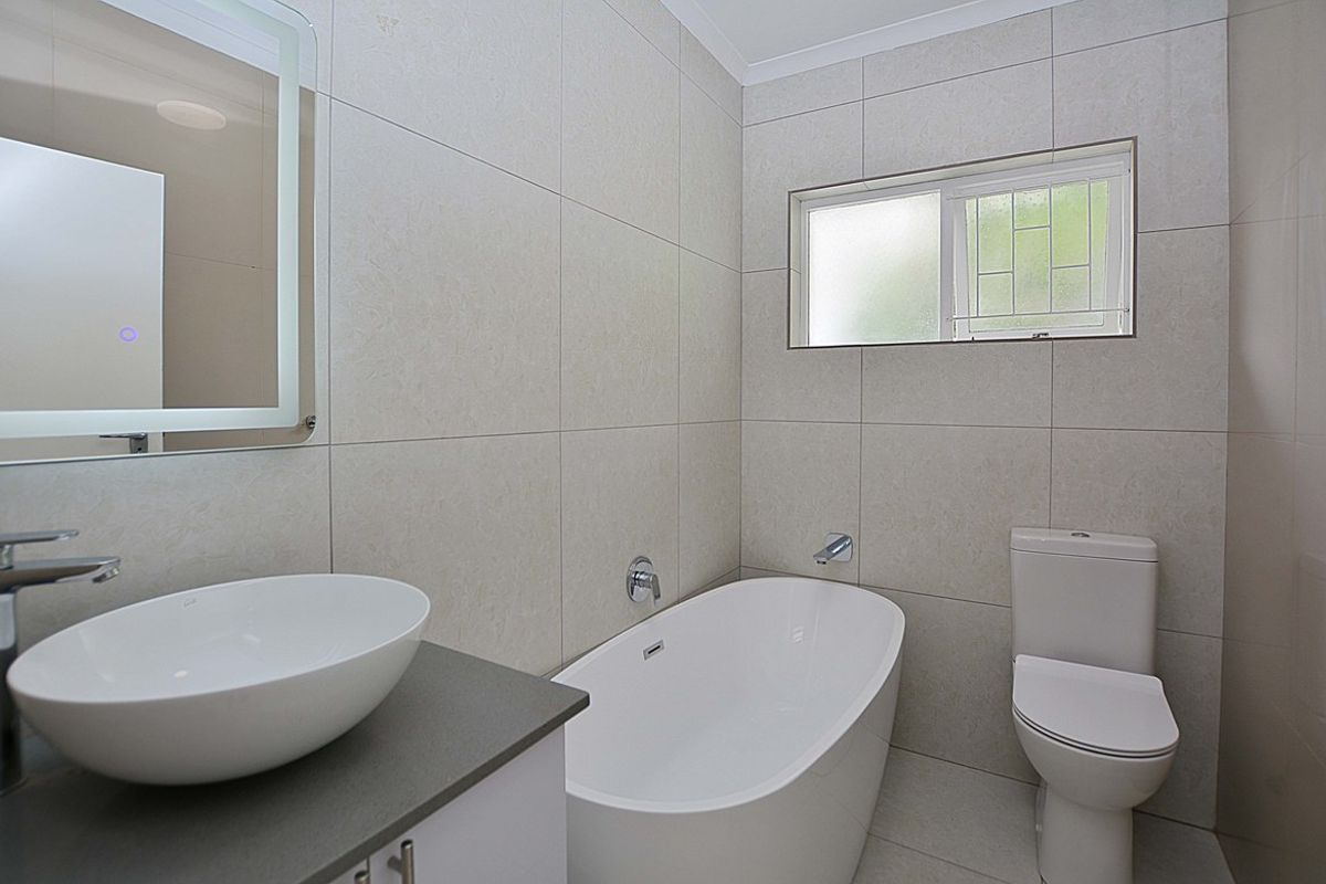 Modern bathroom featuring a freestanding bathtub, a vessel sink vanity, and floor-to-ceiling neutral wall tiles.