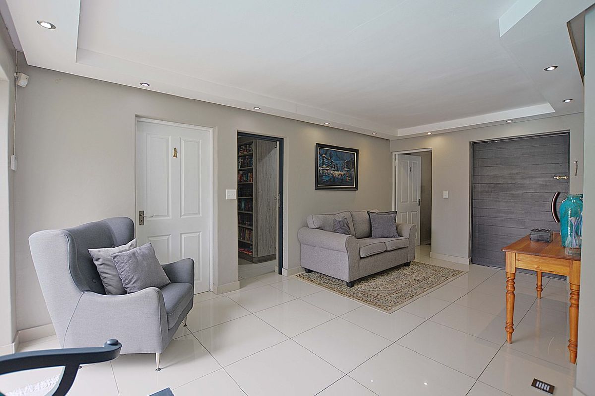 A bright and spacious living area featuring neutral tiled flooring, recessed ceiling lighting, and multiple doorways leading to adjacent rooms.