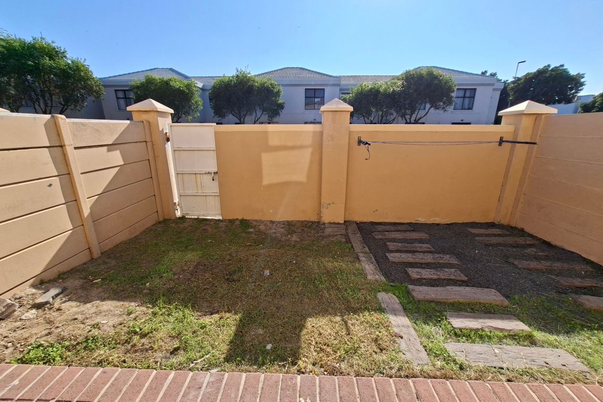 A private rear courtyard featuring a boundary wall, pedestrian gate, paved stepping stones, and a small grassed area.