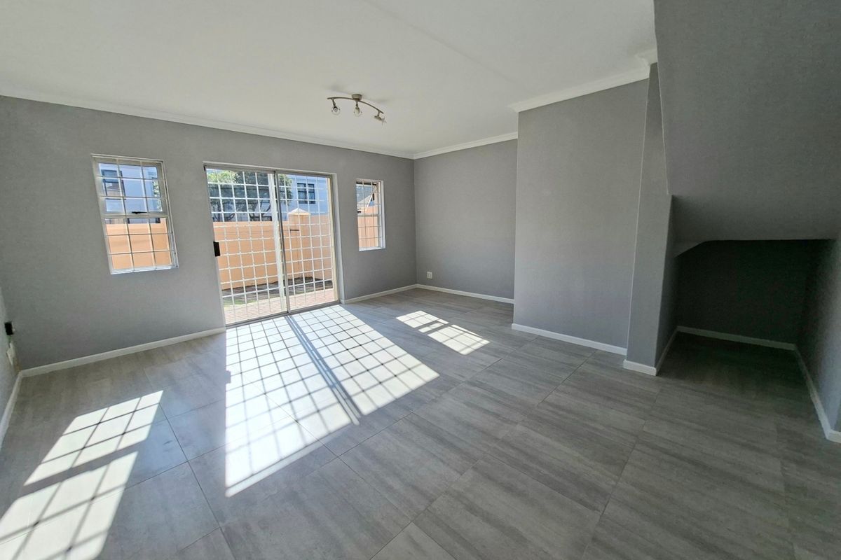 A bright, open-plan living area featuring modern grey floor tiles, neutral walls, and sliding glass doors providing direct access to the rear outdoor space.