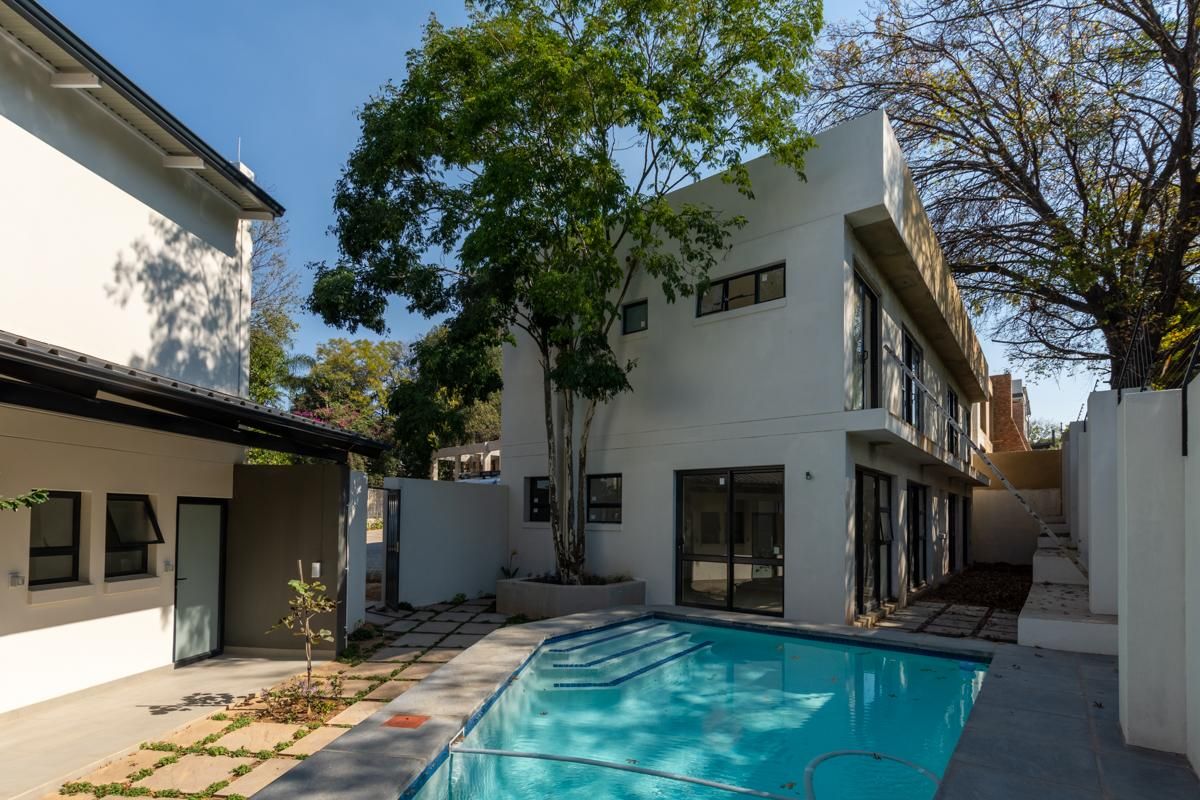 A modern two-story apartment exterior featuring a private swimming pool, paved courtyard area, and clean architectural lines.